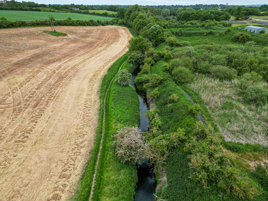 The river running between a ploughed field and grassland